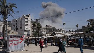 Smoke rises in the sky following an Israeli air strike as Palestinians walk by in Gaza City, 30 May, 2025